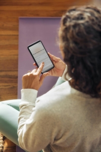 Woman sitting on a yoga mat using an AI chat assistant on her phone, representing how AI fact checking and attention to content quality help ensure the information you rely on is accurate.