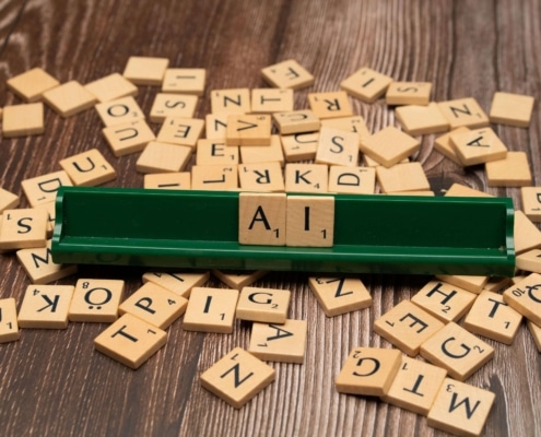 Wooden Scrabble tiles spell out "AI" on a tile rack surrounded by scattered letters. Can AI blogging fully replace the expertise of a human writer? SEO services for therapists combine both, pairing efficiency with genuine clinical insight.