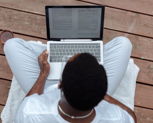Overhead view of a person reading text on a laptop while sitting cross-legged, representing the importance of AI accuracy and carefully reviewing content to catch AI misinformation before publishing.
