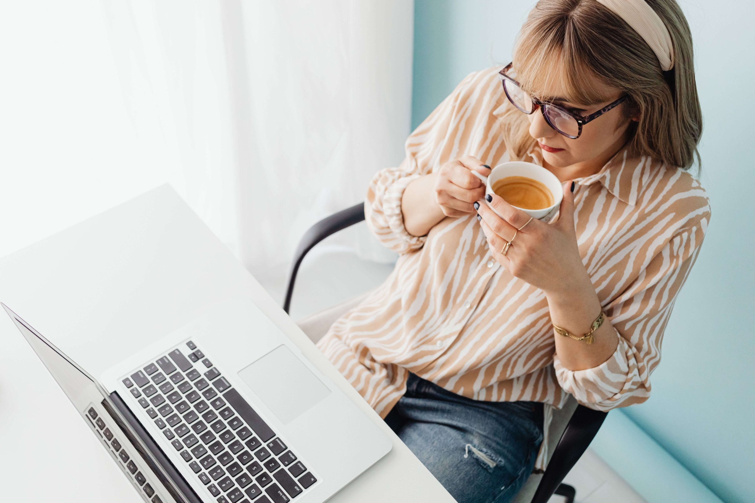 Woman sitting with a cup of tea while using a laptop, representing research, online discovery, and understanding how search engines work.