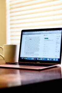 MacBook on a wooden desk displaying a document with editing suggestions next to a coffee mug, representing how content optimization and strong EEAT signals help your writing get understood by both readers and AI.