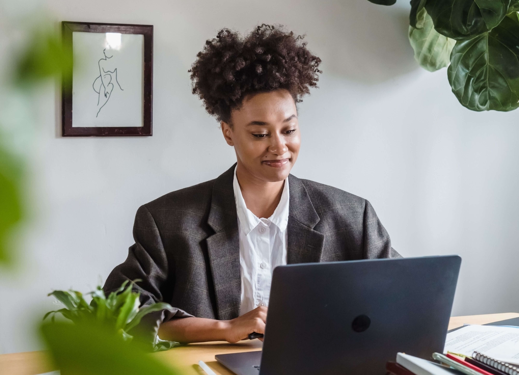Woman in business attire smiling while using a laptop surrounded by plants, illustrating how SEO strategies help businesses improve visibility in search results and AI tools.