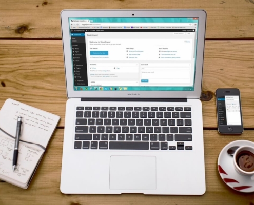 Laptop displaying a WordPress dashboard on a wooden desk next to a notebook, phone, and coffee, representing how good content structure and AI-friendly content start with organizing your website pages clearly.