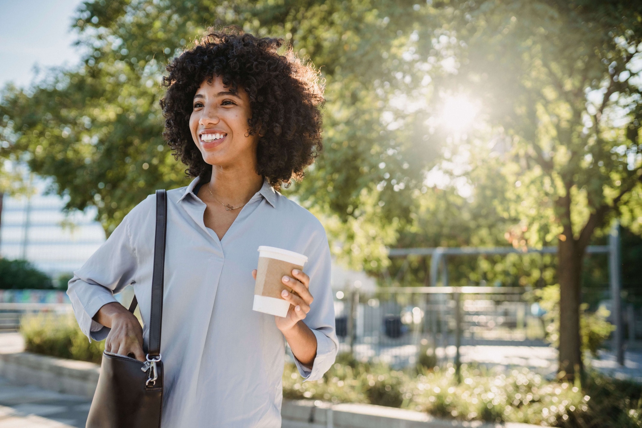 Woman smiling outdoors while holding coffee, representing confidence and a thoughtful approach to building content authority.